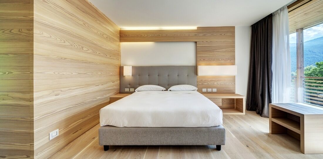 A modern bedroom with a bed, bedside tables, and a large window with a view.
