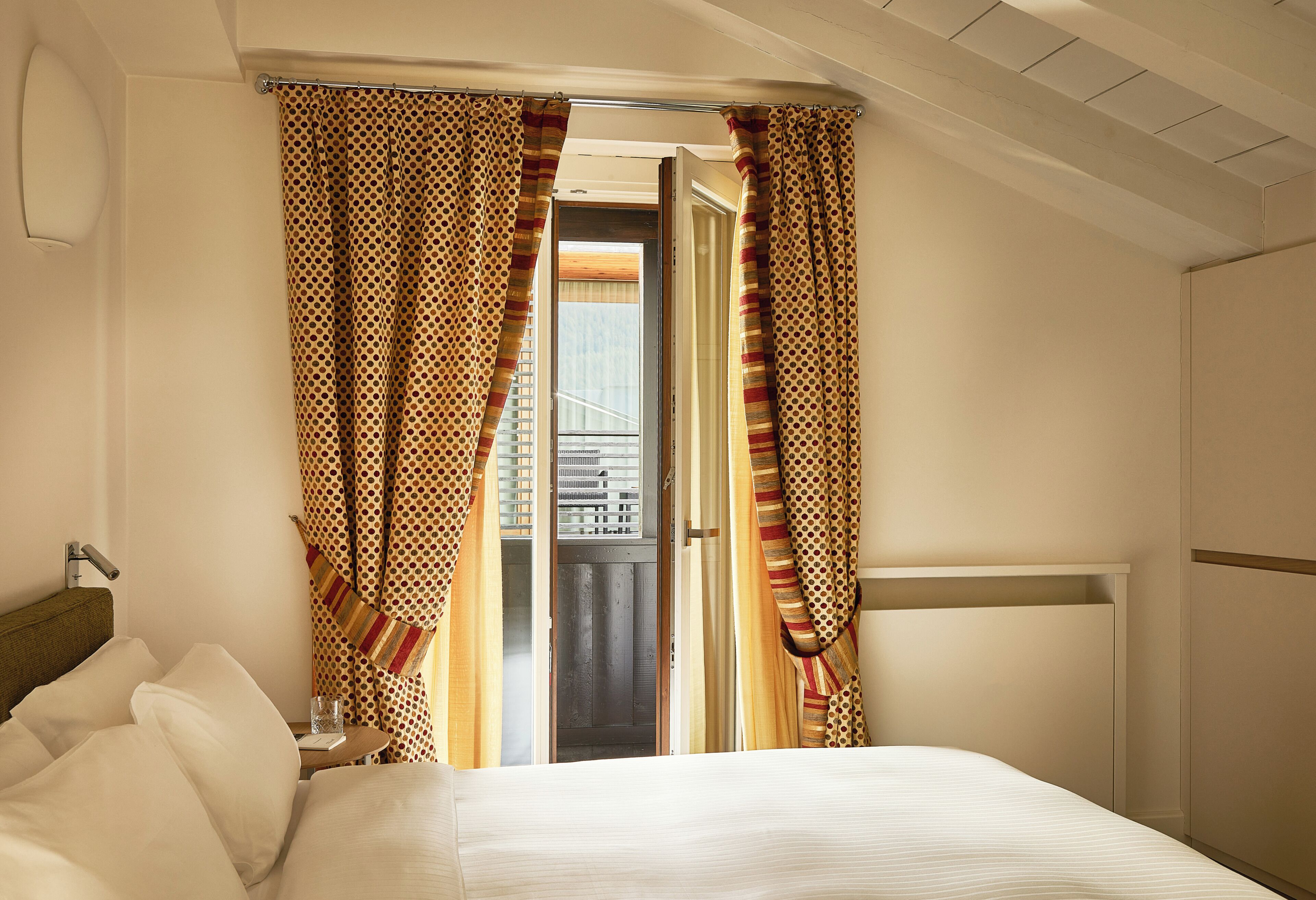Een hotelkamer met een bed, gordijnen, een raam en uitzicht op buiten.