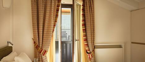 Een hotelkamer met een bed, gordijnen, een raam en uitzicht op buiten.