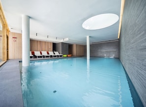 An indoor swimming pool with a clear view of the pool area, including the water, poolside chairs, and the surrounding walls.