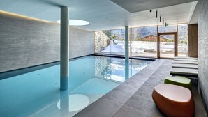 Une piscine intérieure moderne avec des parois en verre transparent, un mur en pierre et une vue sur un paysage enneigé.