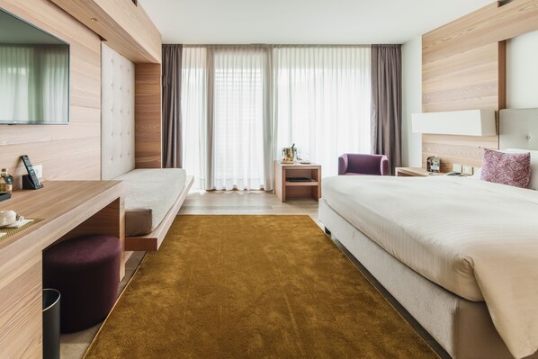 Una habitación de hotel moderna con cama, escritorio, silla, televisor y ventana con cortinas.