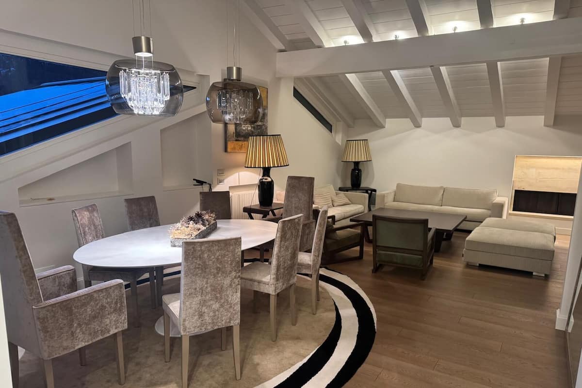 Una sala de estar moderna con una mesa redonda de comedor, varias sillas, un sofá y dos lámparas.