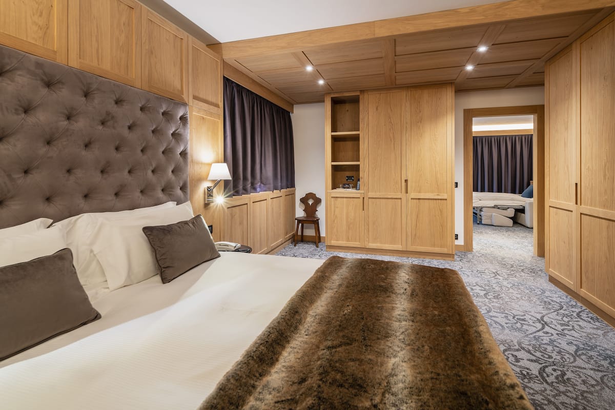 Un dormitorio con cabecera capitonada, cama grande, manta de piel, armario de madera y mesita de noche con lámpara.
