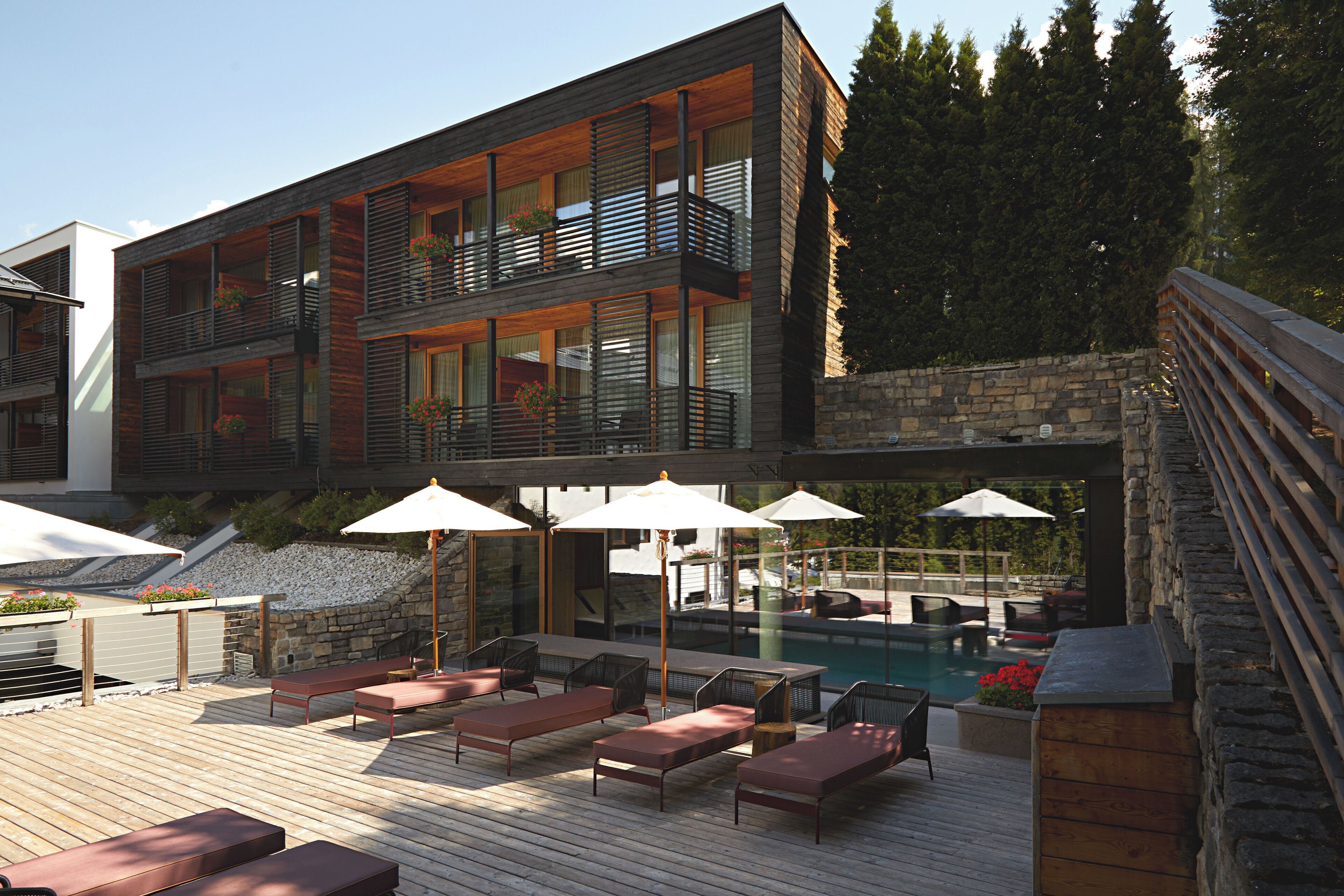 A modern multi-story building with a pool area featuring outdoor seating and umbrellas.