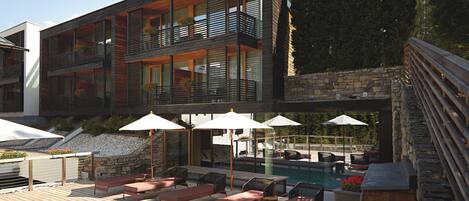 A modern multi-story building with a pool area featuring outdoor seating and umbrellas.