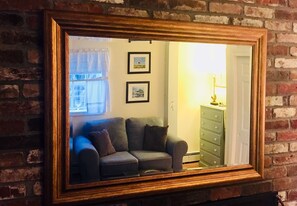 A mirror with a wooden frame reflecting a room with a sofa, a lamp, and a dresser against a brick wall. - Lamb and Lion Inn (Barnstable)