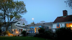Ein zweistöckiges Haus mit einer Terrasse, Sitzgelegenheiten im Freien und einem sichtbaren Mond am Himmel.