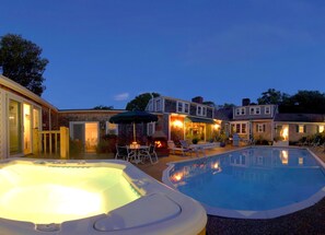 A backyard with a hot tub, a swimming pool, and a patio area with chairs and a table. - Lamb and Lion Inn (Barnstable)
