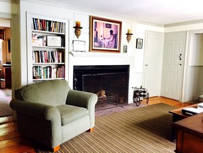 A living room with a fireplace, bookshelves, a green armchair, and a coffee table.