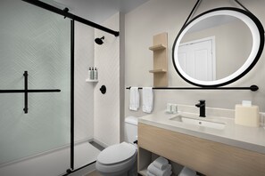 Een moderne badkamer met een douchecabine van glas, toilet, wastafel met spiegel en een handdoekhouder.