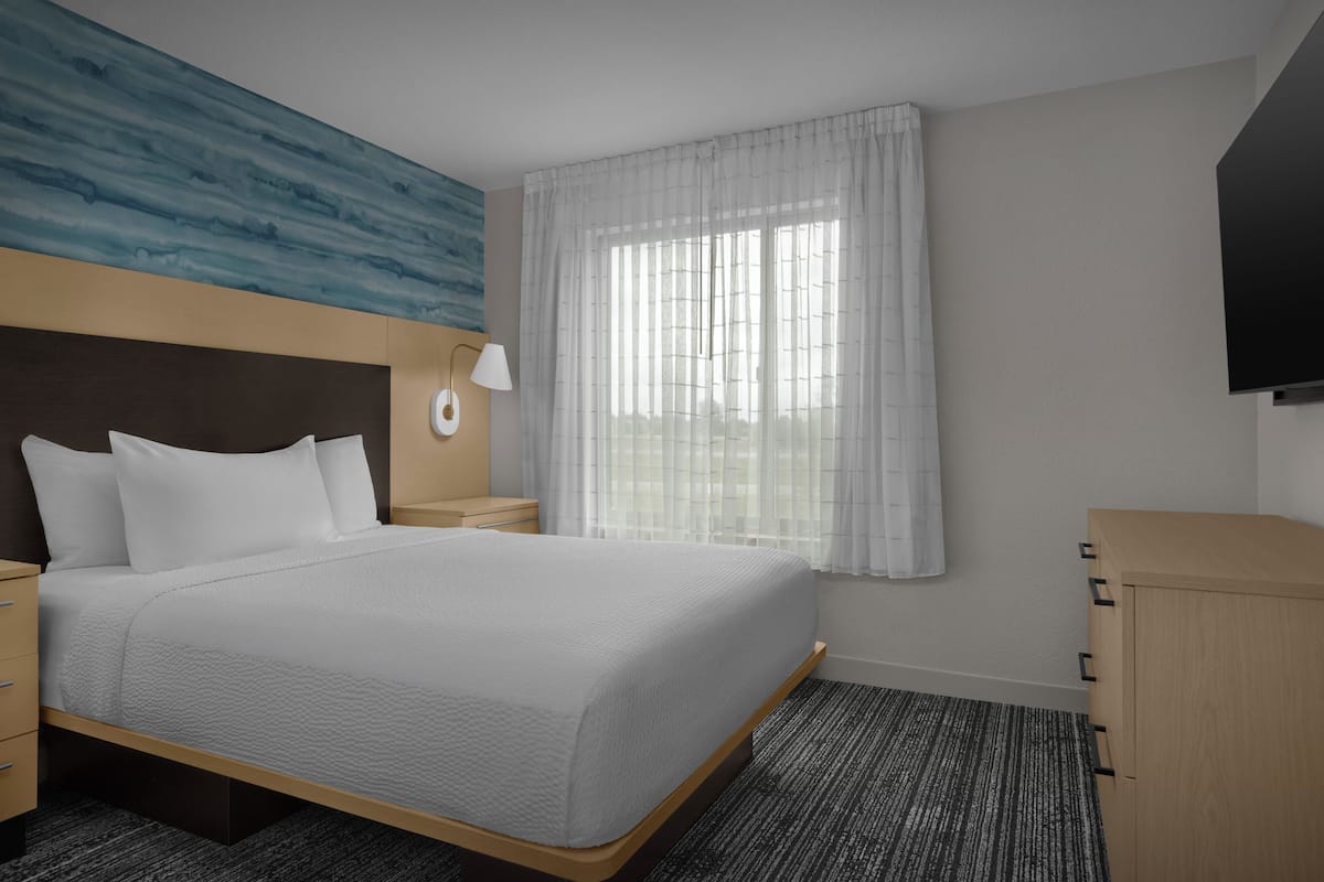 A hotel room with a bed, bedside table, lamp, and a wardrobe.