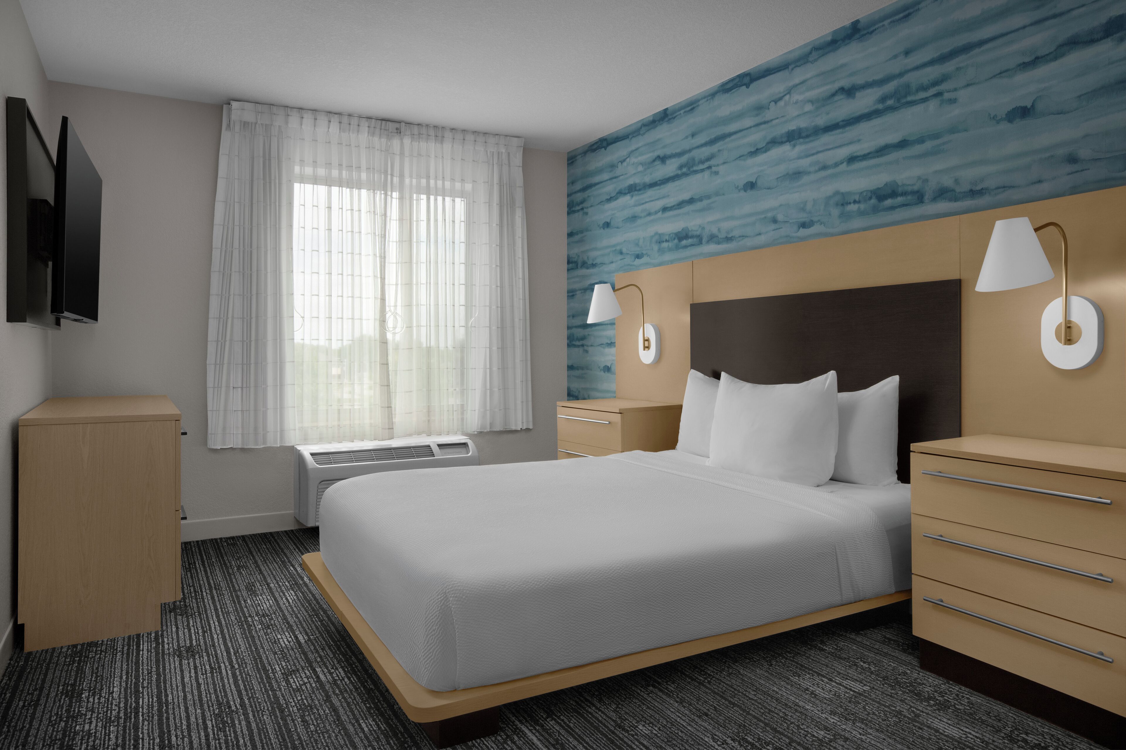 Habitación de hotel con cama, escritorio, cómoda, televisión y ventana con cortinas.