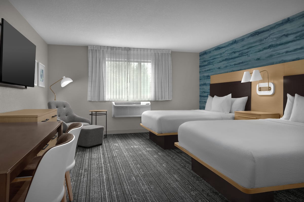 A hotel room with two beds, a desk, a chair, a lamp, and a window with curtains.
