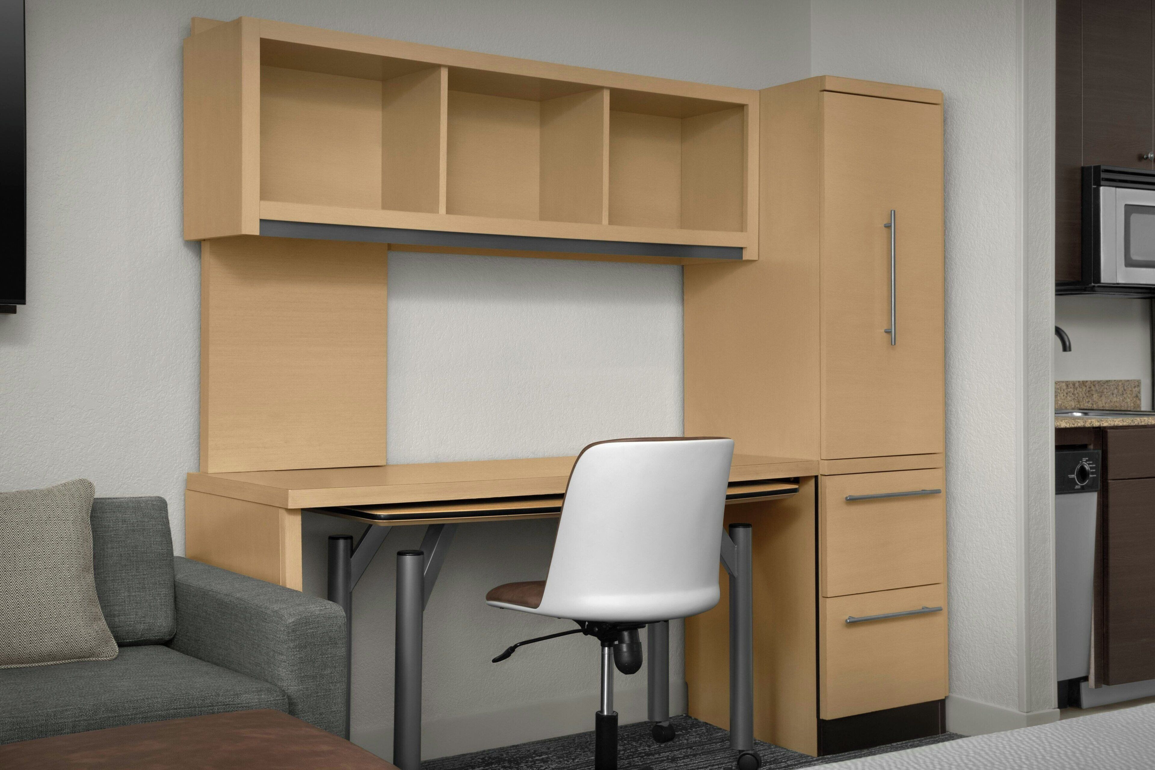A compact room with a desk, chair, and a kitchenette area.