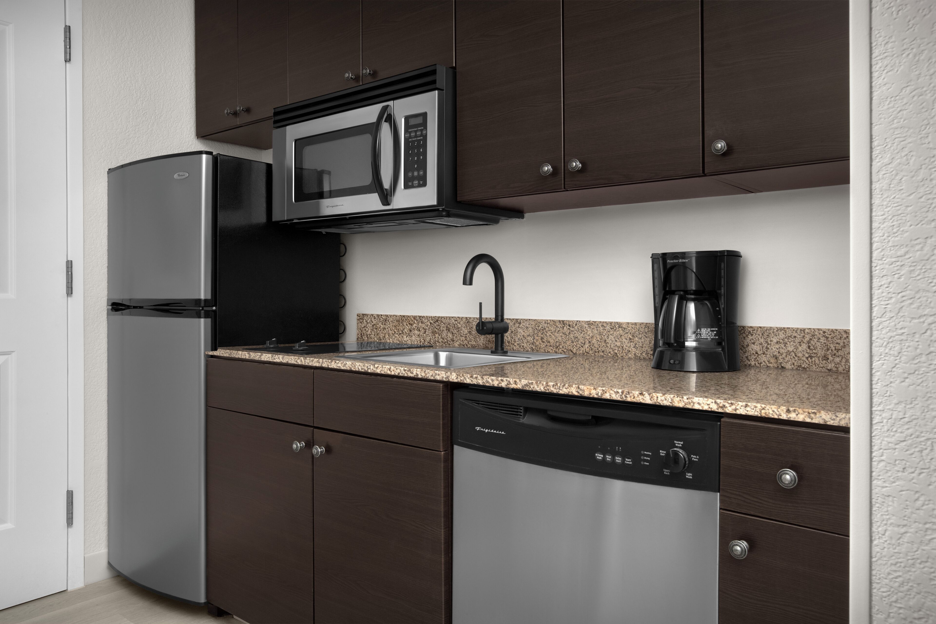 Une cuisine moderne dotée d’appareils électroménagers en acier inoxydable, d’un plan de travail en granit et de meubles de rangement aux couleurs sombres.