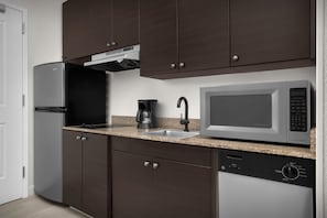 Una cocina moderna con armarios marrón oscuro, un refrigerador de acero inoxidable, un microondas integrado y un lavavajillas.
