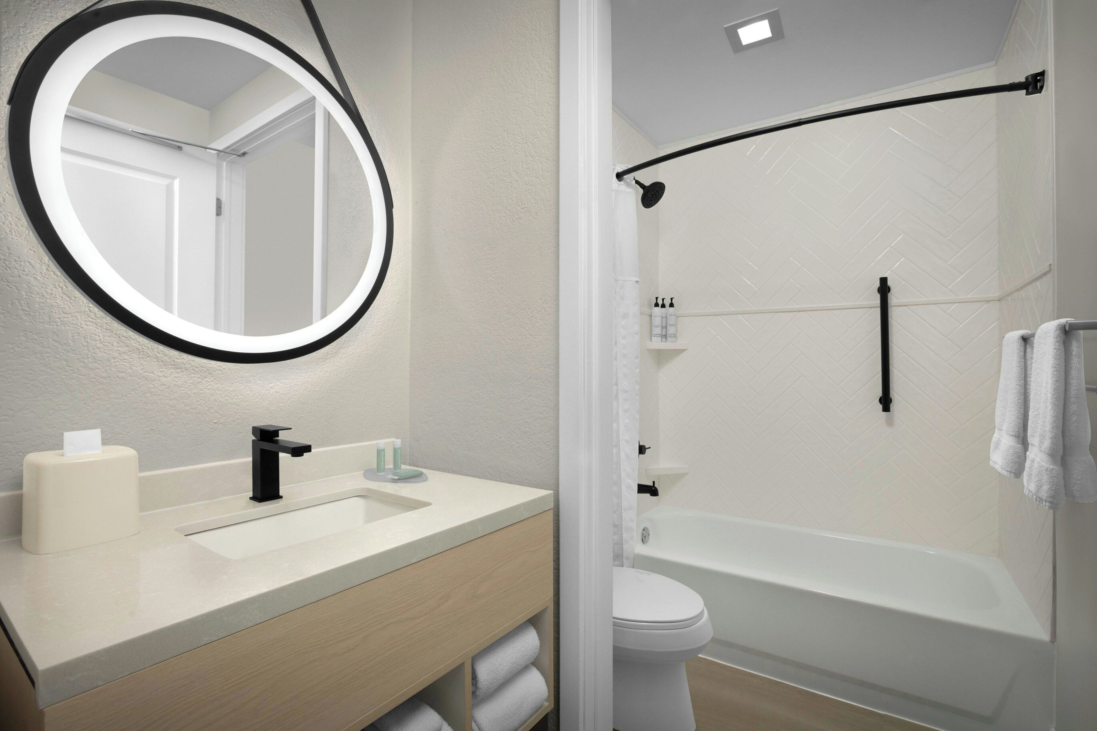 Une salle de bain avec un miroir rond, un lavabo, des toilettes et une baignoire.