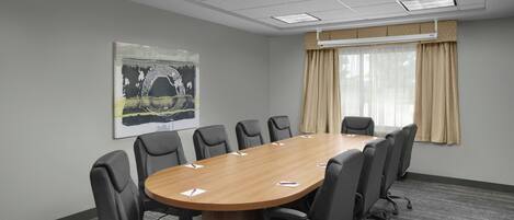A conference room with a long table, black chairs, a large abstract painting, and a window with curtains.