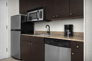 Uma cozinha moderna com eletrodomésticos de aço inoxidável, bancada de granito e armários escuros.
