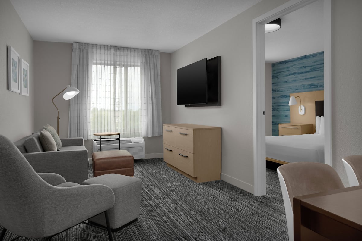 A modern hotel room with a sofa, a desk, a flat-screen TV, a wooden dresser, and a bed with a blue wall mural.