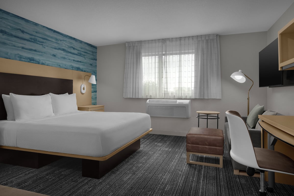 A hotel room with a large bed, a desk, a chair, a TV, a lamp, and a window with curtains.