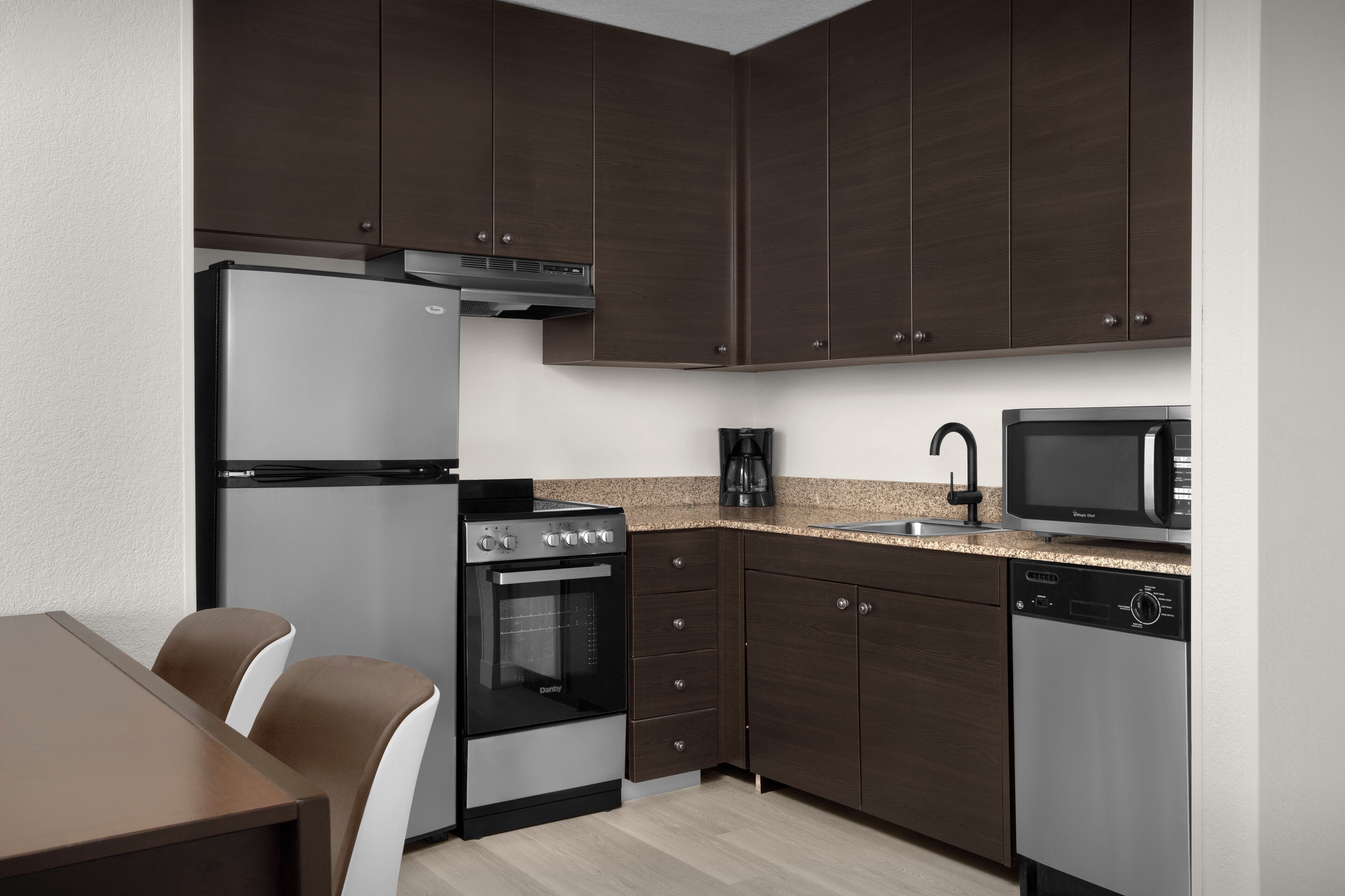 A modern kitchen with dark wooden cabinets, a stainless steel refrigerator, an oven, a microwave, and a dishwasher.