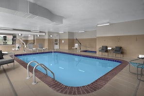 Une piscine intérieure avec des bords carrelés, un vestiaire doté d’un miroir et un espace détente avec des chaises.