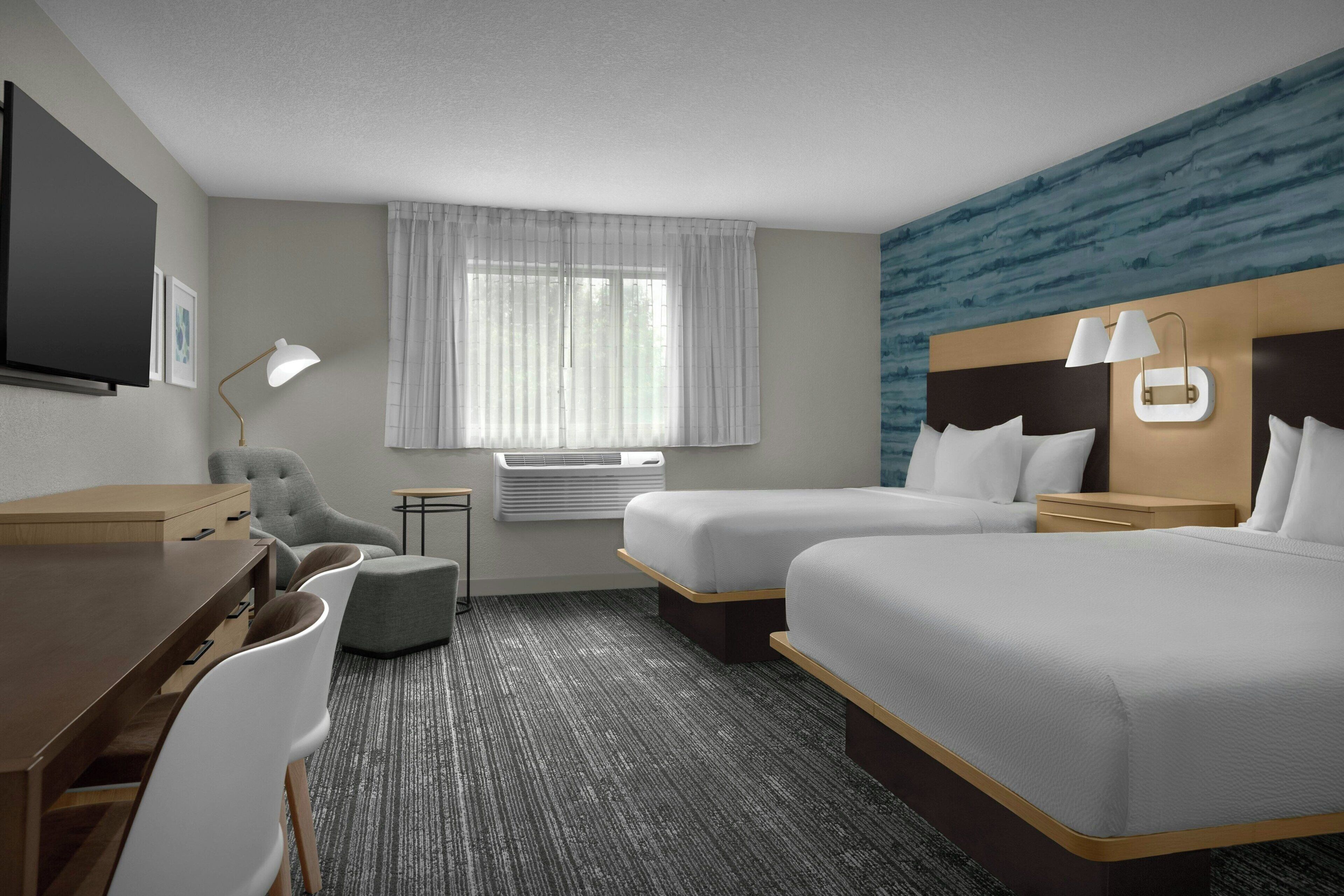 A hotel room with two beds, a desk, a chair, a lamp, and a window with curtains.