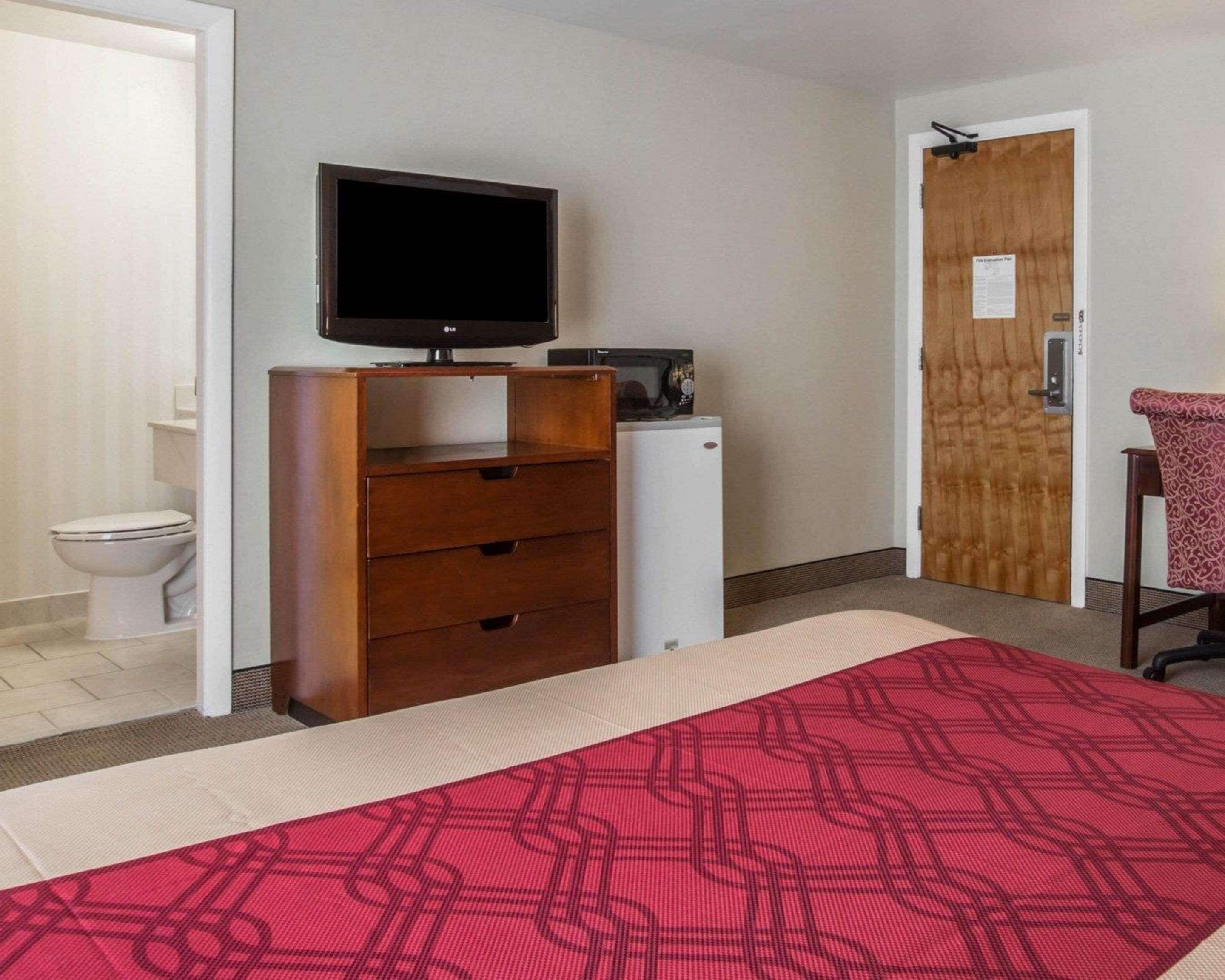 Ein Schlafzimmer mit Bett, Kommode, Fernseher, einer Tür und einer Toilette.