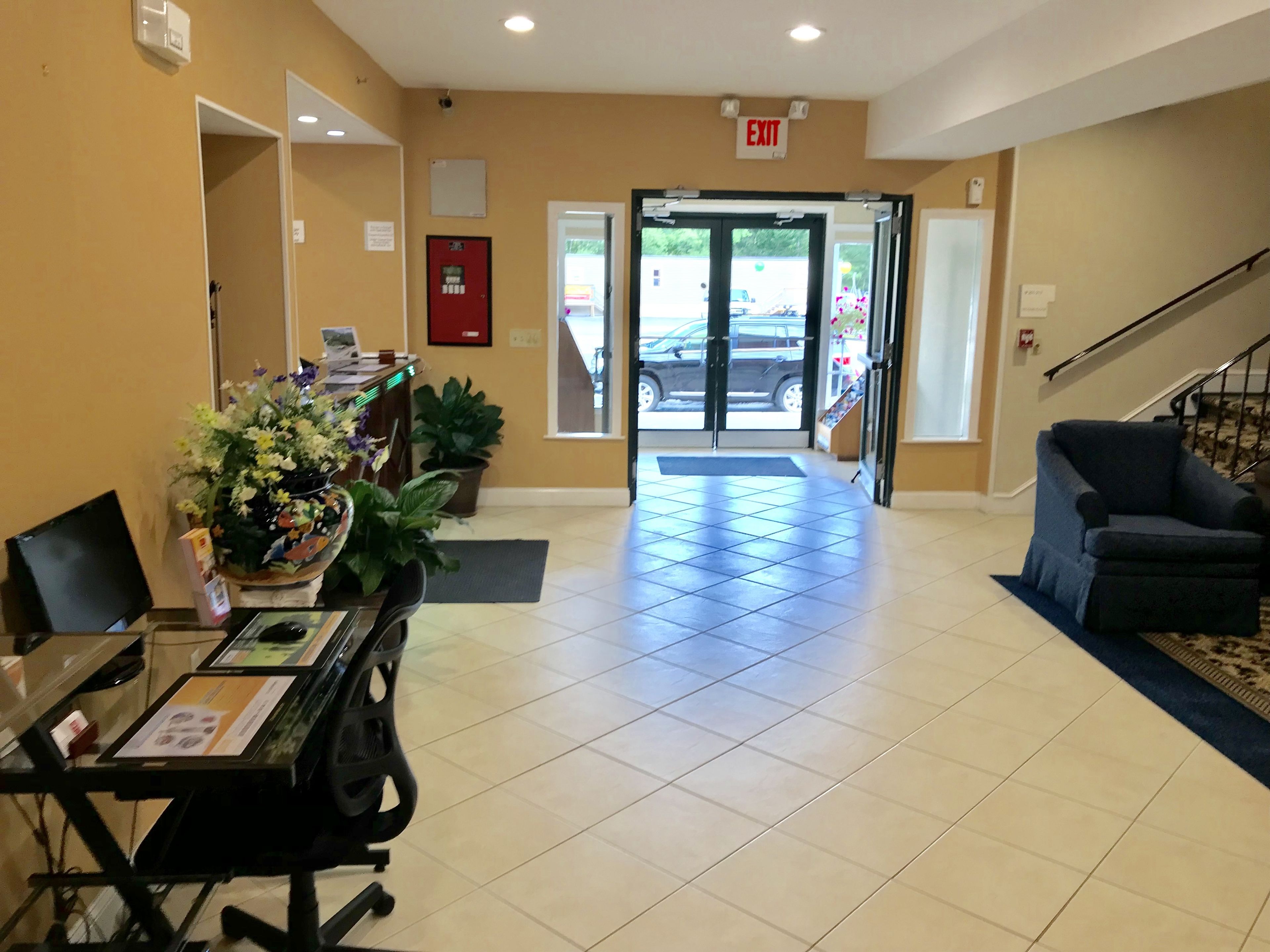A reception area with a desk, chairs, a potted plant, and a blue armchair. - Econo Lodge Lake Region (West Ossipee)