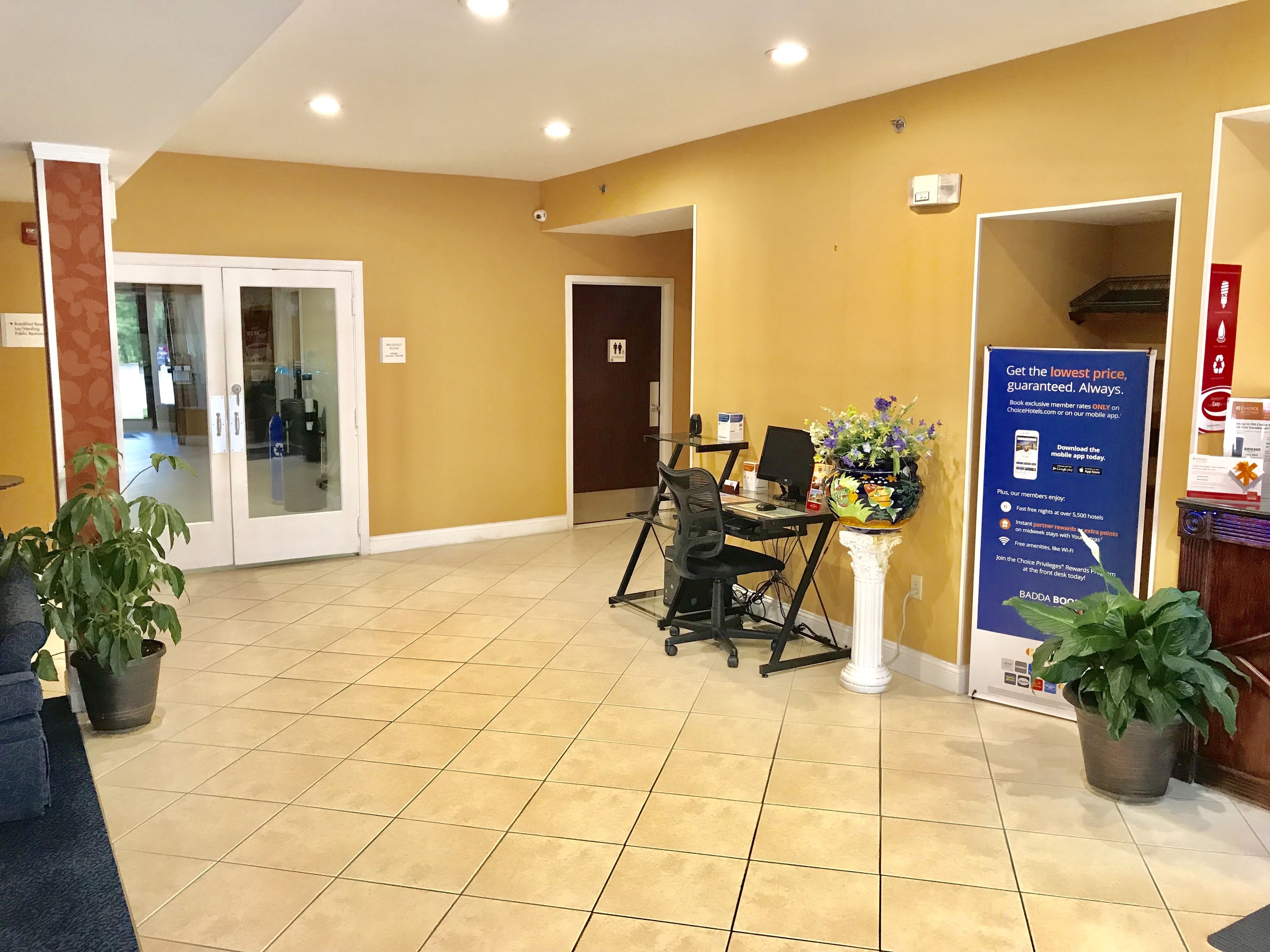 A reception area with a desk, chairs, a potted plant, and a signboard.