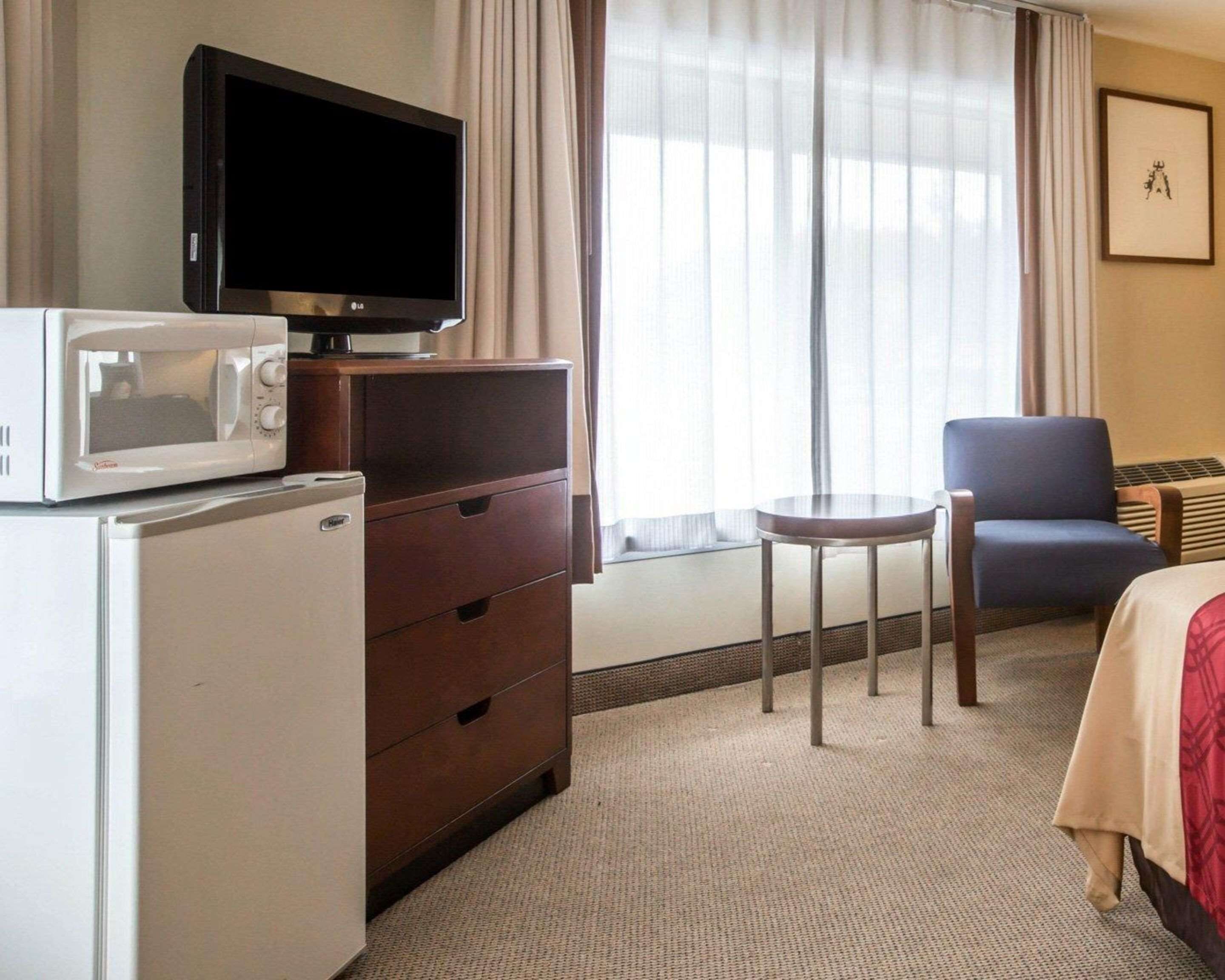 A hotel room with a flat-screen TV, a microwave, a small table, a chair, and a bed.