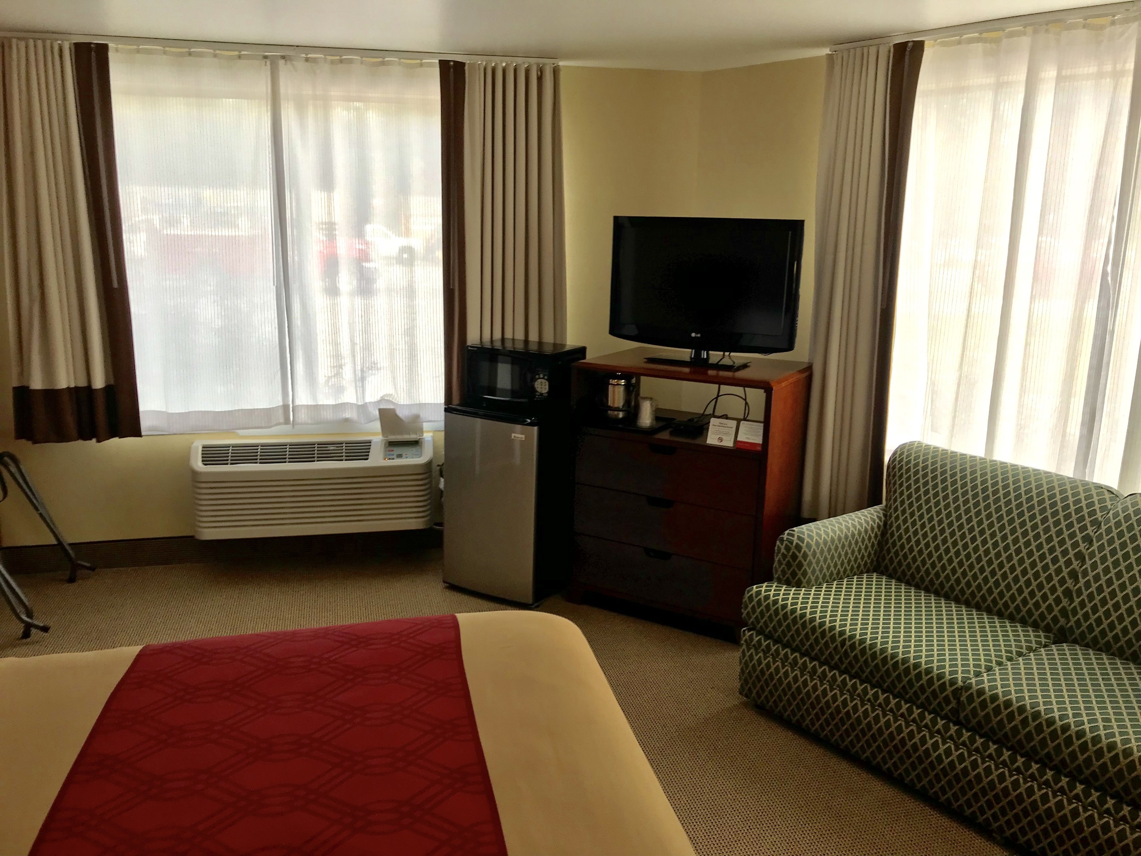 Una habitación de hotel con cama, sofá, televisión, minibar, calefacción y cortinas.