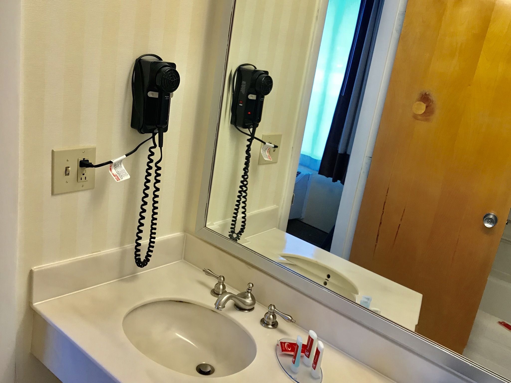 A bathroom with a sink, mirror, and hair dryer mounted on the wall.