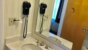 A bathroom with a sink, mirror, and hair dryer mounted on the wall.