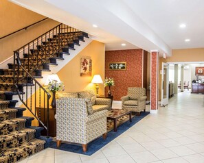 A hotel lobby with a staircase, patterned sofas, a coffee table, and a vase with flowers. - Econo Lodge Lake Region (West Ossipee)