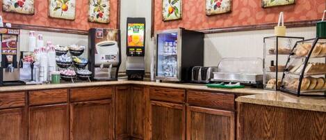 Een ontbijtbuffet met koffieautomaten, een drankenspender en een display met gebak.