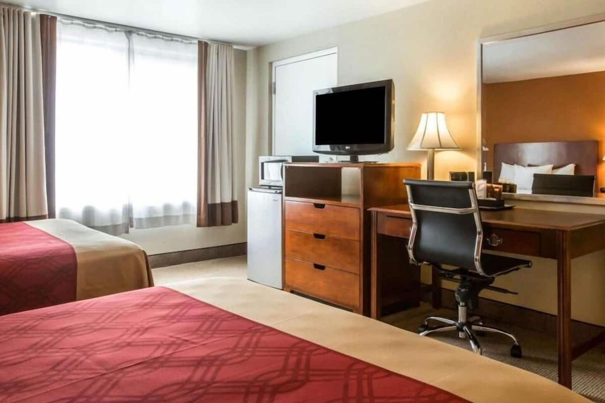 A hotel room with two beds, a desk, a television, and a lamp.