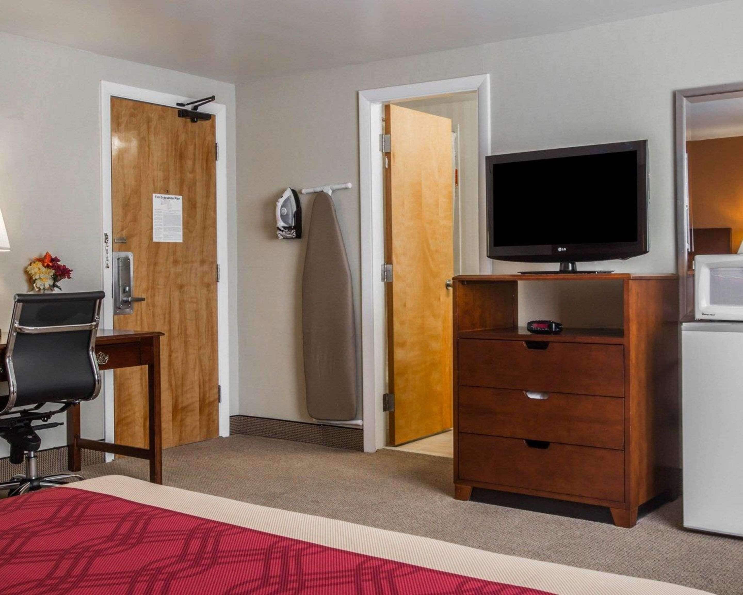 A hotel room with a bed, a desk with a chair, a television, a microwave, and a refrigerator.
