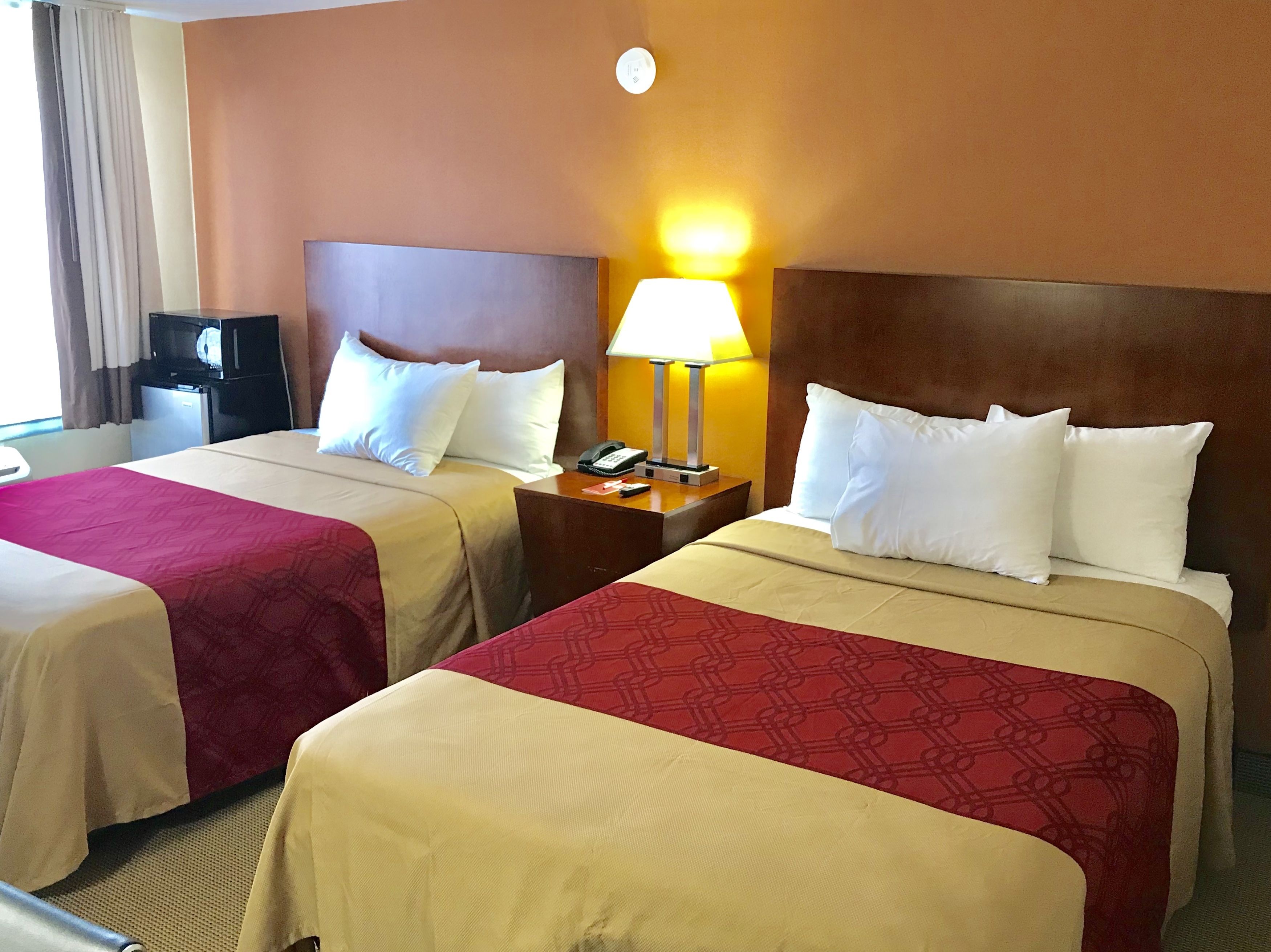 Hotellihuone, jossa on kaksi sänkyä, ja jokaisessa sängyssä on pääty sekä yöpöytä lampun ja puhelimen kanssa.