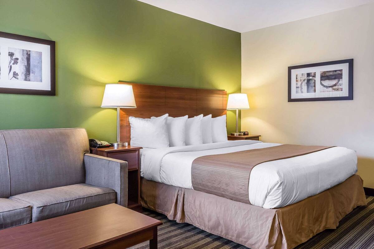 A hotel room with a bed, a sofa, a nightstand, and two wall-mounted lamps.