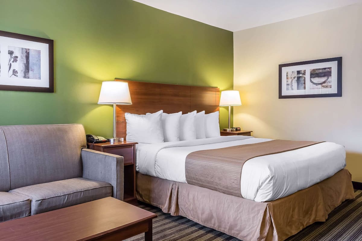 A hotel room with a bed, a sofa, a nightstand, and two wall-mounted lamps.