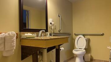 A bathroom with a sink, mirror, towel rack, toilet, and handrails.