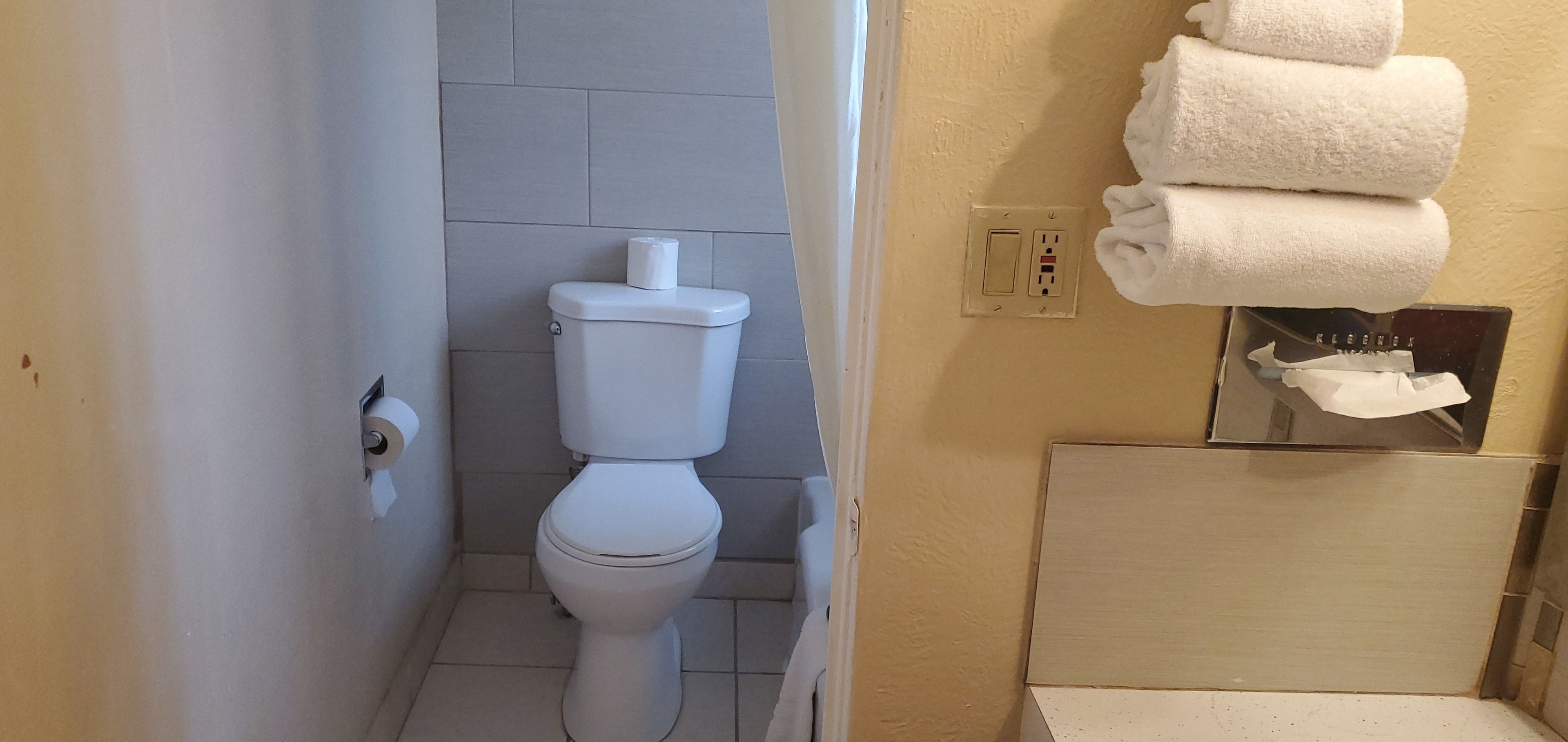 A small bathroom with a toilet, a towel rack with folded towels, and a mirror.