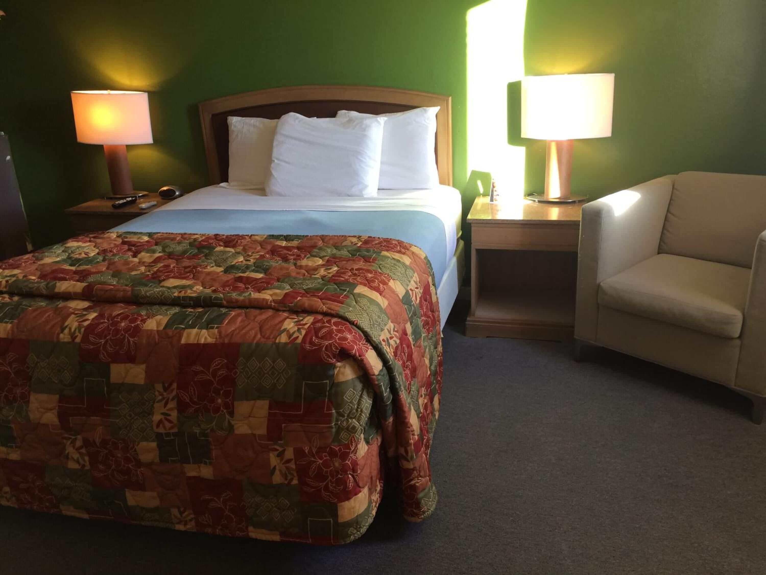 A hotel room with a bed, two bedside lamps, a chair, and a nightstand.