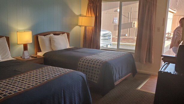 Une chambre d’hôtel avec deux lits, une table de chevet avec une lampe et une vue sur l’extérieur grâce à une grande fenêtre.
