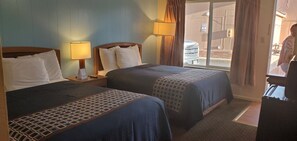 A hotel room with two beds, a nightstand with a lamp, and a view of the outside through a large window. - Alamo Motel (Sheridan)