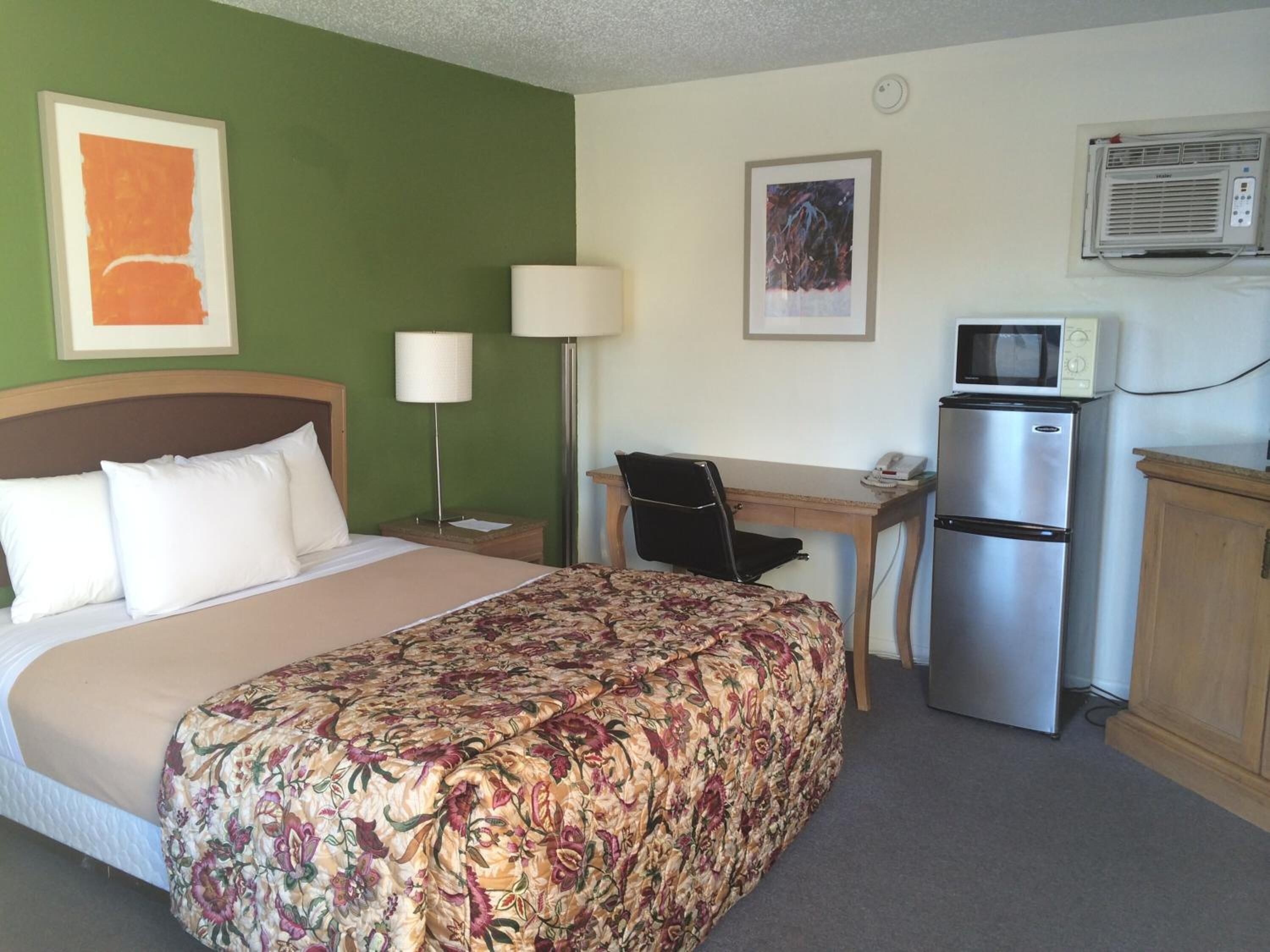Una habitación de hotel con cama, escritorio, silla, refrigerador y microondas.