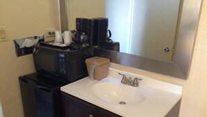Une salle de bain avec un lavabo blanc, un meuble en bois foncé et un miroir au-dessus du lavabo. On y trouve également une machine à café et un four à micro-ondes sur le comptoir.